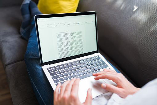 Adult man typing a letter or essay on the word processor in his laptop while resting on the couch