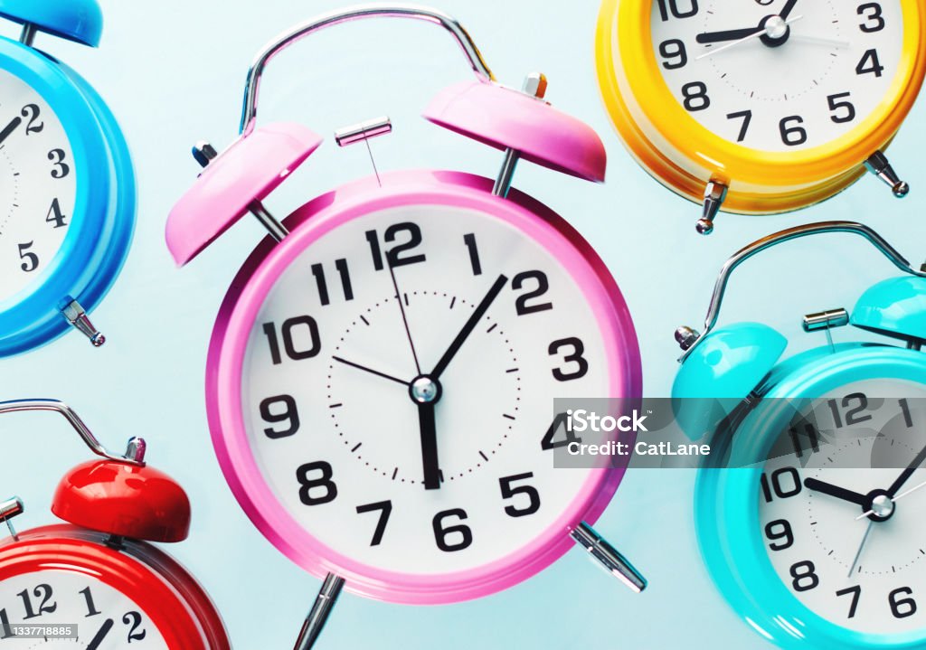 Assorted Collection of Colorful Alarm Clocks Each Showing a Different Time Clock Stock Photo