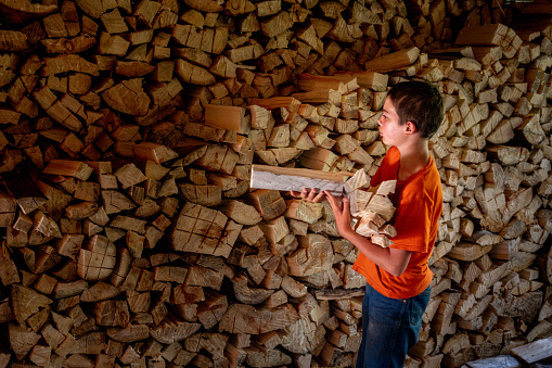 A male worker is standing and working in a lumber storage area