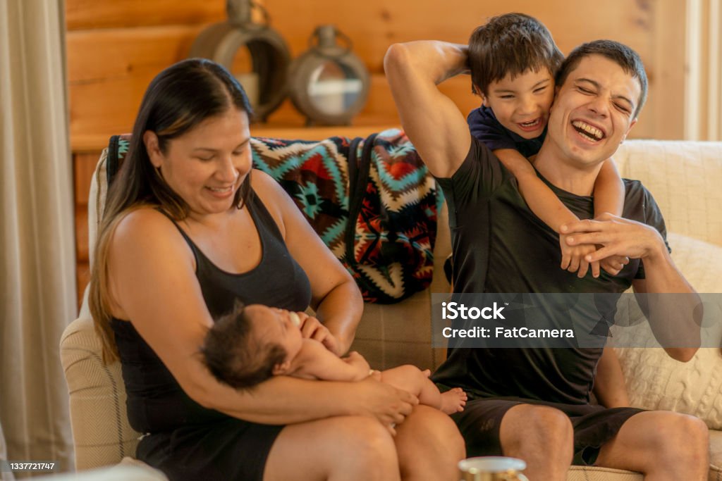 Young Indigenous family of two spending quality time together A beautiful young Indigenous family spending quality time together at home. They are seated on a sofa in their living room. Indigenous Peoples of the Americas Stock Photo