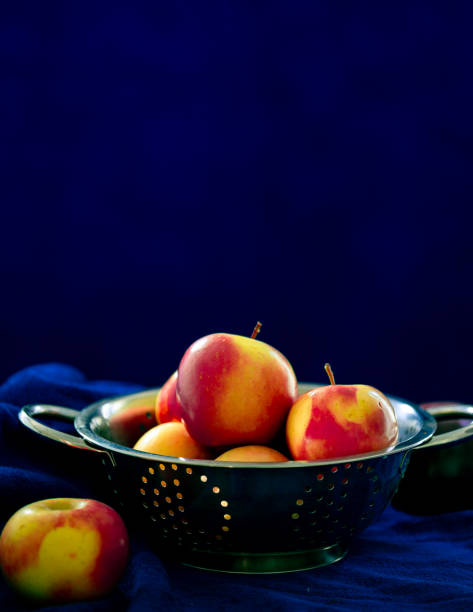 Fresh apples in a colander against blue background.