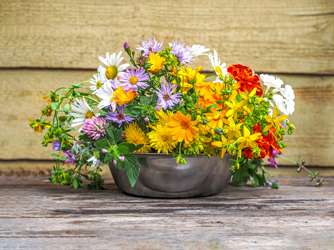 A variegated bouquet of summer wildflowers in a metal cup close-up on a porch of a village house
