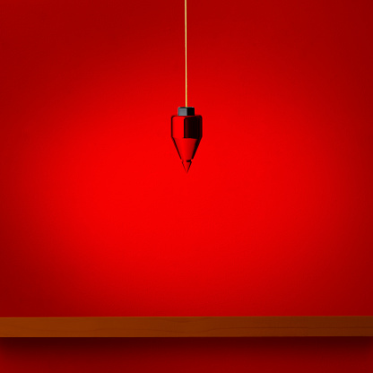 Hanging a plumb bob over the wooden shelf against red wall.