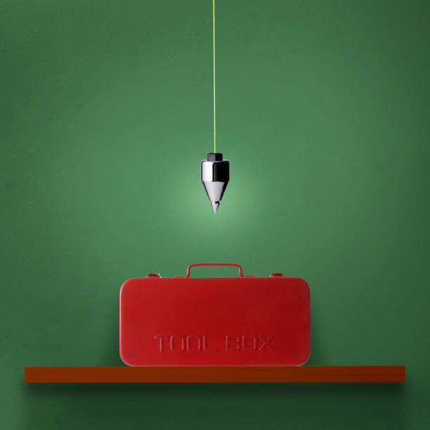 Hanging a plumb bob over the wooden shelf with red toolbox against green wall.