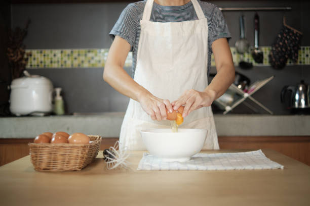 istock Female cook in a white apron is cracking an egg in home's kitchen. 1337738705
