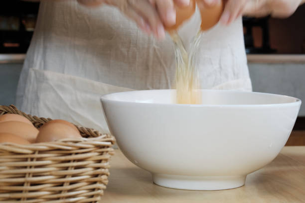 흰 앞치마를 입은 여성 요리사가 집 부엌에서 달걀을 부수고 있습니다. - eggs bowl cracked dining table 뉴스 사진 이미지