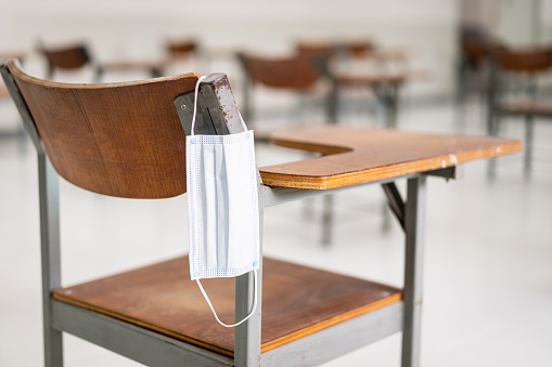 Una mascarilla médica usada cuelga de una silla de conferencia de madera en el aula vacía durante la pandemia de COVID-19 photo