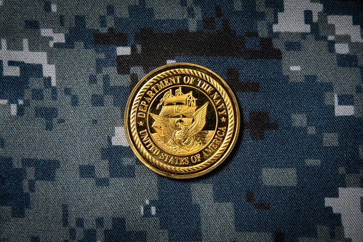 A US Navy gold coin on the Navy digital camo uniform background.