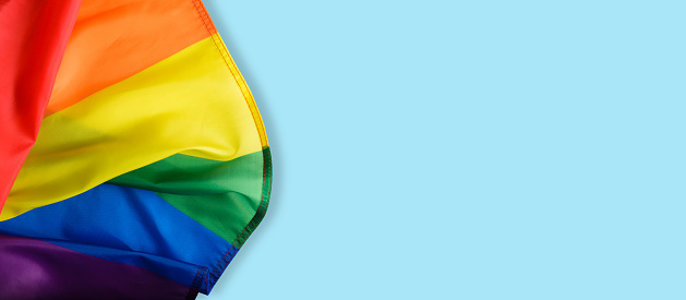 Rainbow flag on light blue background, international symbol of LGBT community top view. Banner, copy space.
