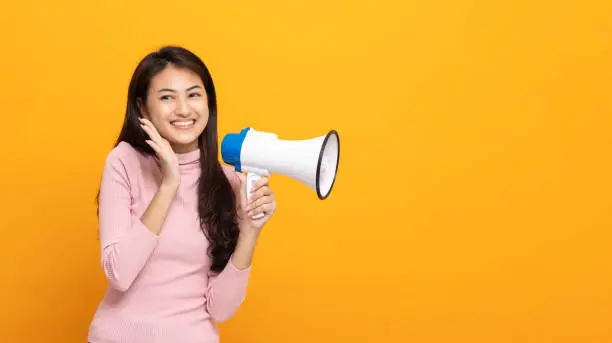 Photo of Shout out loud with megaphone. Young beautiful asian woman woman announces with a voice about promotions and advertisements for products at a discounted price. Shopping and fashion concept.