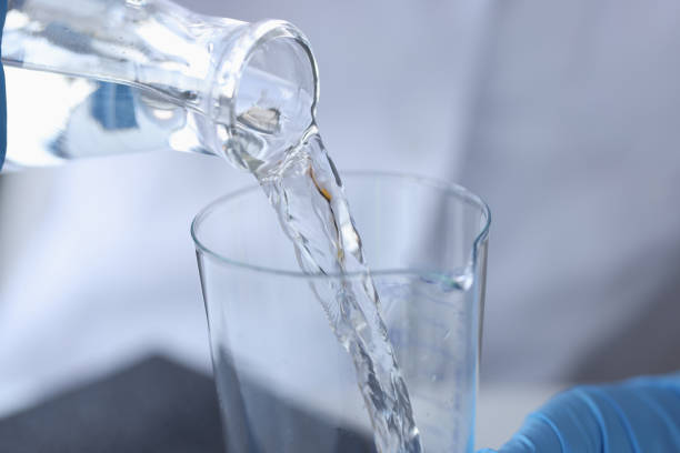 wissenschaftler chemiker gießt wasser aus transparenter flasche in kolben in labornahaufnahme - mint liquor stock-fotos und bilder