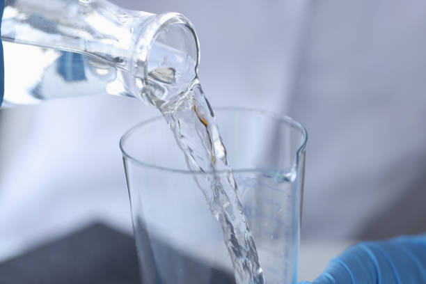 un chimiste scientifique verse de l’eau d’une bouteille transparente dans une fiole en gros plan en laboratoire - textile scientific experiment laboratory textile industry photos et images de collection