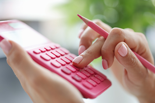 Woman hand holding pink pencil and counting on calculator closeup. Home bookkeeping concept