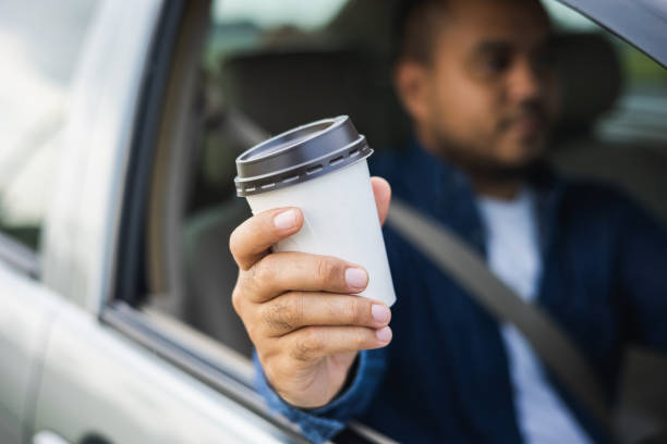 istock Young man drinking a cup of hot coffee while driving car to travel. Hands holding steering wheel. 1337751663