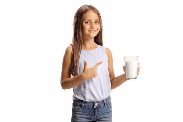 pretty little girl holding a glass of milk and pointing - milk child drinking little girls imagens e fotografias de stock