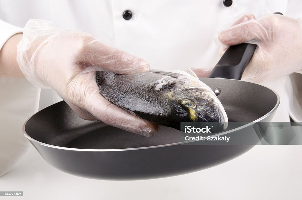 female chef holds a sea bream female chef puts a sea bream for frying in a pan Adult Stock Photo