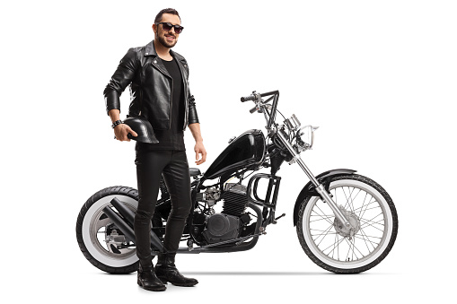 Full length portrait of a biker with a chopper holding helmet and wearing sunglasses isolated on white background