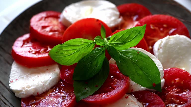 Caprese salad. Tomato salad with mozzarella and basil leaves. Italian cuisine. Mediterranean lunch. Organic food. Italian caprese