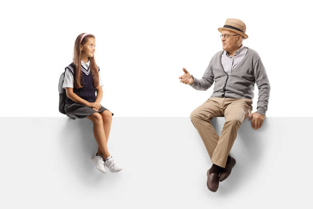 istock Grandfather and a schoolgirl seated on a blank panel and talking 1337765193