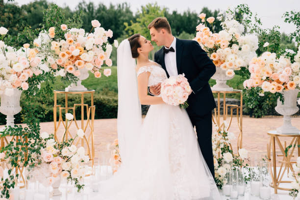 bride and groom in the wedding ceremony area of live white and pink flowers. beautiful bride and groom in the wedding ceremony area of live white and pink flowers. decoration and organization of celebrations in the open air. natural arch photos stock pictures, royalty-free photos & images