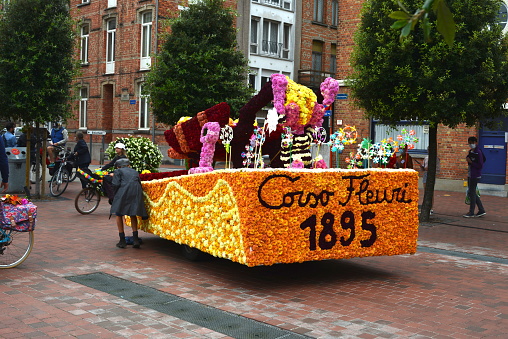 Blankenberge,  Belgium - August 29, 2021: festival carnival floral parade . Group Corso Fleuri 1895 riding circles on an antique bicycle around the flower float.