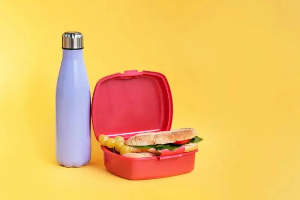 Reusable bottle and plastic sandwich box on bright yellow background. Sustainability at home, work and school concept