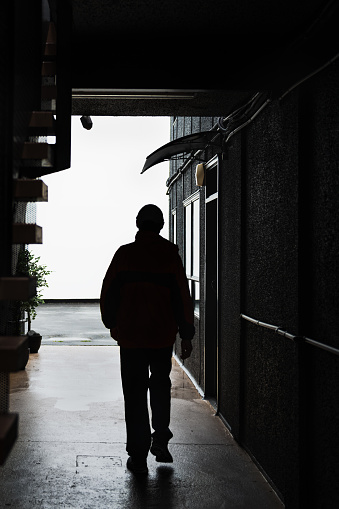 Silhouette of a man walking alone in a dark narrow archway. Vertical format.