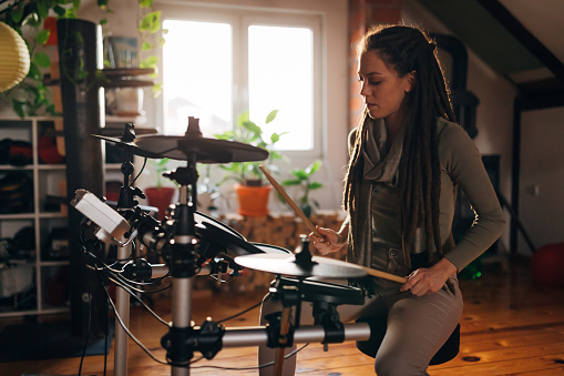 Urban modern female drummer, playing drums in her cozy home music studio