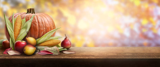 istock A thanksgiving celebration table of pumpkins, apples, pears and corncobs with autumn sunset foliage in the background. 1337778294