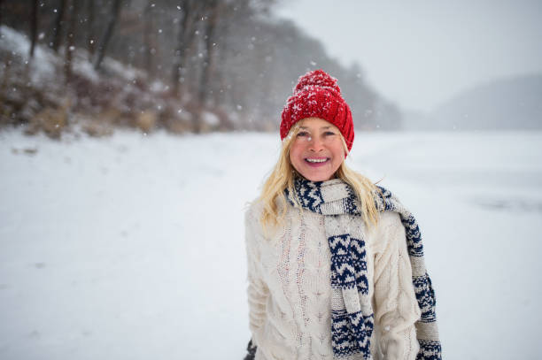 retrato da visão frontal de uma mulher idosa feliz com chapéu ao ar livre em pé na natureza nevada, olhando para a câmera. - scarf women hat warm clothing - fotografias e filmes do acervo