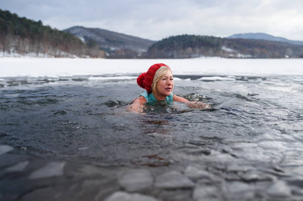 Front view of active senior woman swimming outdoors in water in winter, cold therapy concept. A front view of active senior woman swimming outdoors in water in winter, cold therapy concept. woman cold water swimming stock pictures, royalty-free photos & images
