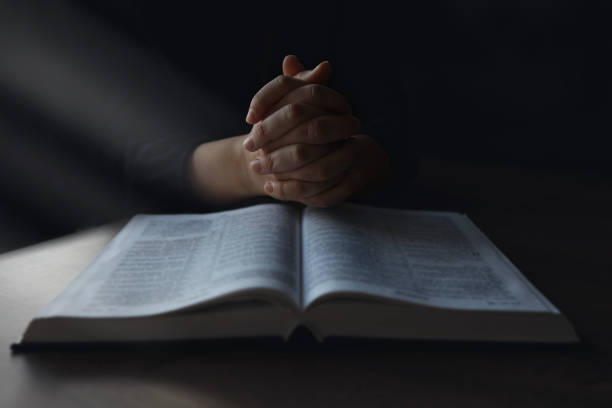 la mujer manos en la biblia. ella está leyendo y orando sobre la biblia en un espacio oscuro sobre una mesa de madera - reading religious text black bible fotografías e imágenes de stock
