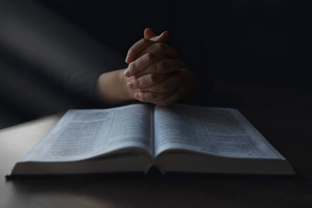 woman hands on bible. she is reading and praying over bible in a dark space over wooden table - prayer call imagens e fotografias de stock