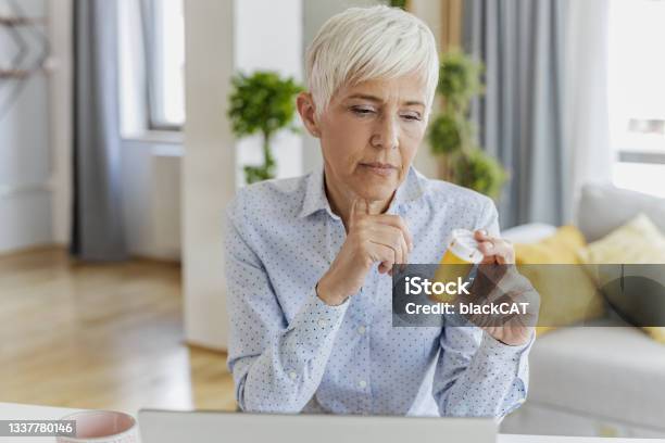 Worried Senior Woman Holding A Bottle Of Medicine In Her Hand Stock Photo - Download Image Now