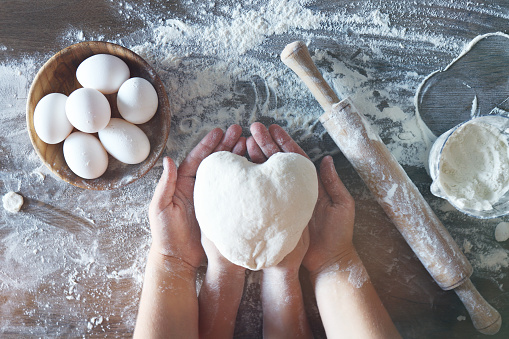 Mother and child hands prepares the dough with flour on wooden table. In the hands of a heart of dough