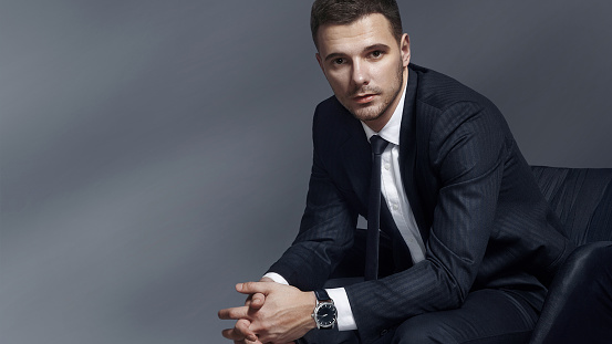 Elegant man on a gray background studio with a clock in a suit There is free space for your advertisement.