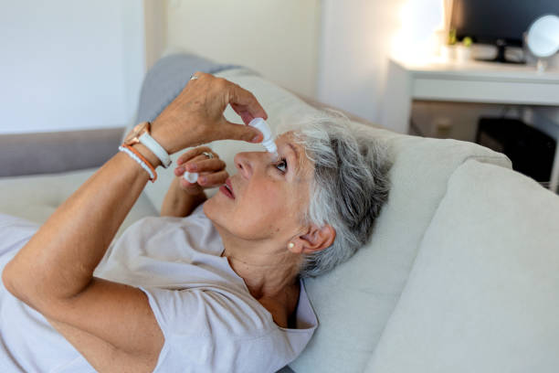Closeup view at an elderly women using a bottle of eyedrops due to ophthalmic problems.