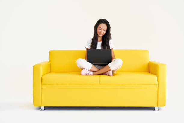 istock Pretty smiling woman using laptop sitting on yellow couch on white background 1337793499