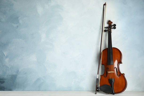 istock Beautiful violin and bow on white wooden table near light blue wall. Space for text 1337795419