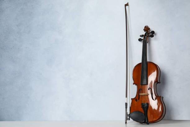 istock Beautiful violin and bow on table near light blue wall. Space for text 1337795474