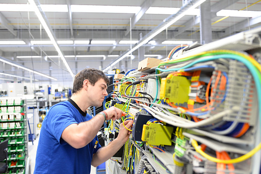 joven aprendiz ensambla componentes y cables en una fábrica en un armario de conmutación - industria del lugar de trabajo con futuro photo