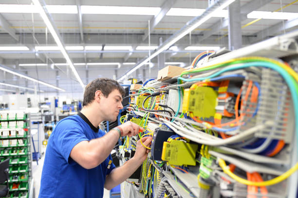 giovane apprendista assembla componenti e cavi in una fabbrica in un quadro elettrico - l'industria del posto di lavoro con il futuro - operaio di produzione foto e immagini stock