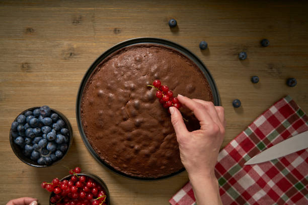 istock Woman decorates handmade chocolate cake with blackberries and red currants. 1337804621