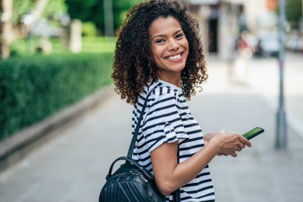 Portrait of beautiful happy woman Portrait from behind of beautiful afro american woman with smartphone walking on city street and looking over shoulder one young woman only stock pictures, royalty-free photos & images