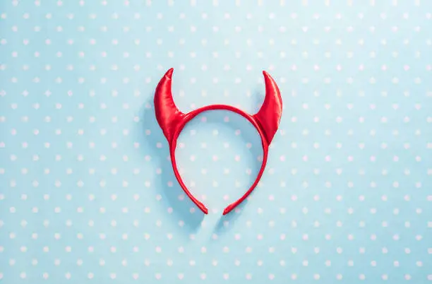Red devil horns on a headband hoop. Halloween texture background.