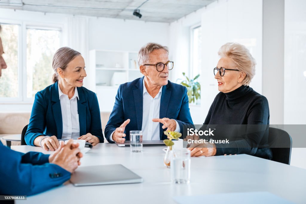 Senior business people during meeting Senior businesswomen and businessmen wearing elegant suits sitting at the table in the office and discussing during business meeting. Shareholder Stock Photo