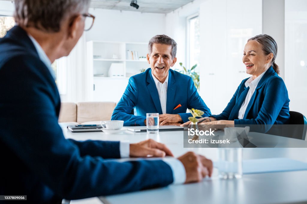 Senior business people during meeting Senior businesswomen and businessmen wearing elegant suits sitting at the table in the office and discussing during business meeting. Senior Women Stock Photo