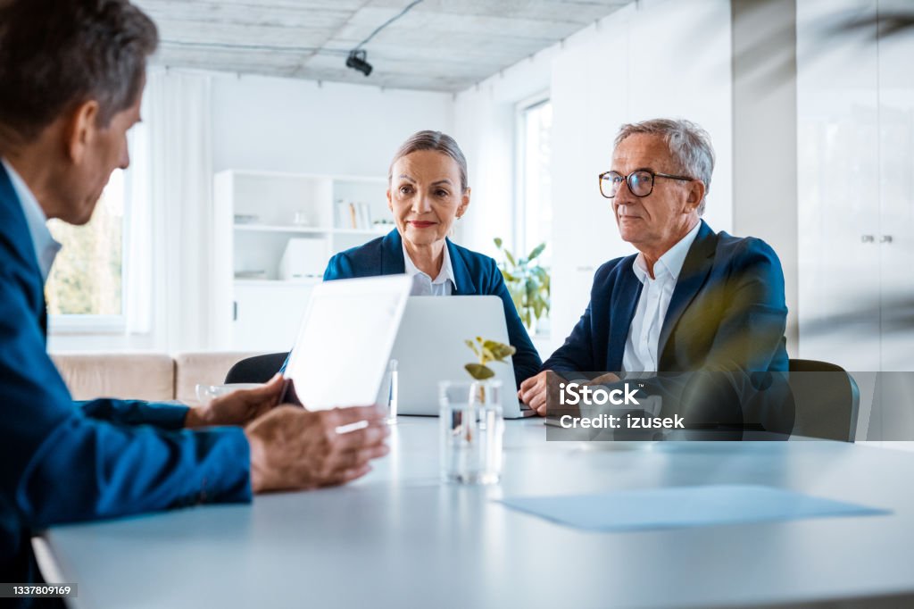Senior business people during meeting Senior businesswomen and businessmen wearing elegant suits sitting at the table in the office and discussing during business meeting. Office Stock Photo