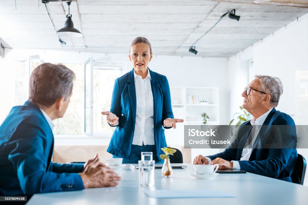 Senior business people during meeting Senior businesswomen and businessmen wearing elegant suits sitting at the table in the office and discussing during business meeting. Senior Adult Stock Photo