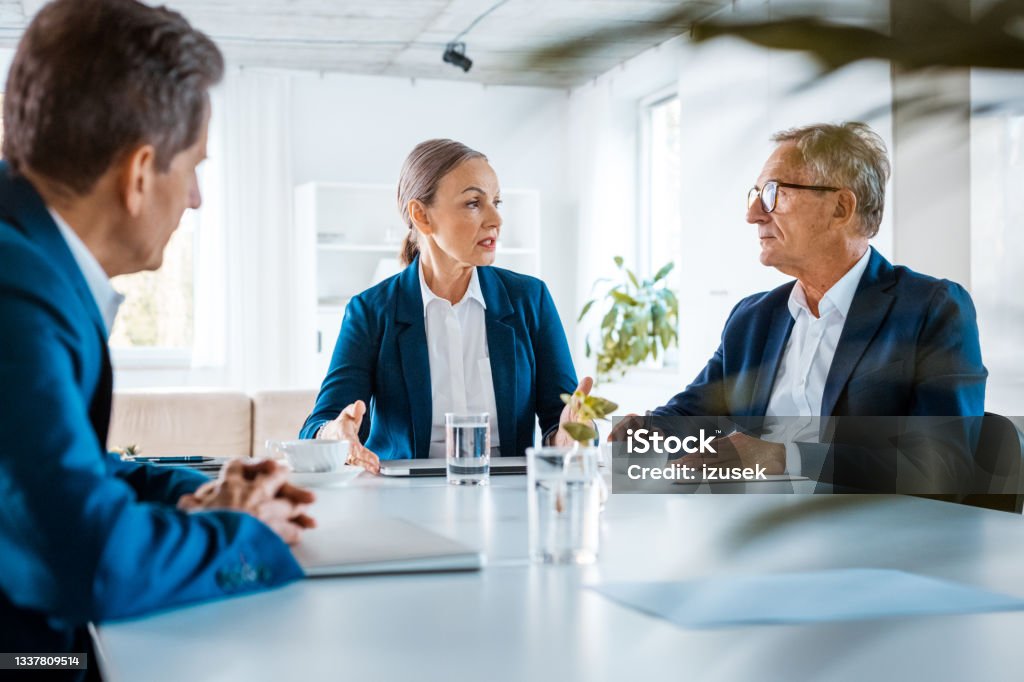 Senior business people during meeting Senior businesswomen and businessmen wearing elegant suits sitting at the table in the office and discussing during business meeting. Agreement Stock Photo